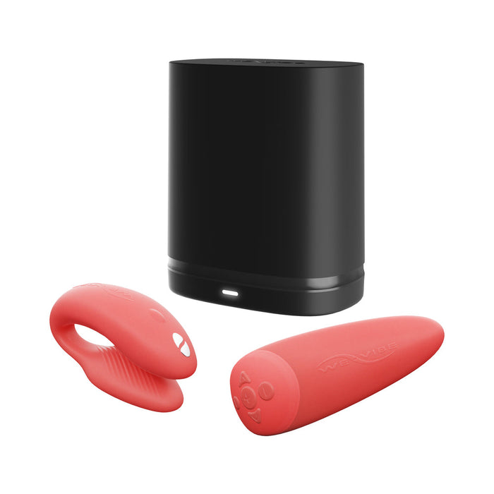 The We-Vibe Chorus Remote & App Controlled Couples' Vibrator in Coral, featuring both ring and elongated shapes with control buttons and smooth surfaces for an adjustable fit, is displayed in front of its black charging case.