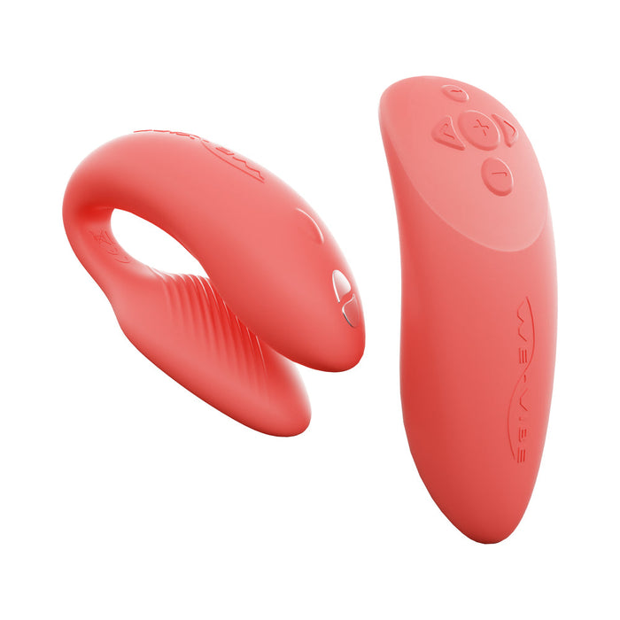 The We-Vibe Chorus Remote & App Controlled Couples' Vibrator in coral pink features a flexible, curved silicone design for adjustable fit, shown with a matching wireless remote with multiple buttons.