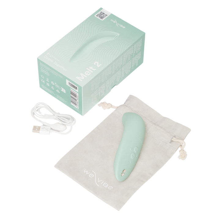 A mint green We-Vibe Melt 2 Rechargeable Pleasure Air Clitoral Stimulator is shown on a drawstring pouch with its USB charging cable and product box, all displayed against a white background.