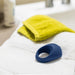 A We-Vibe Pivot Vibrating Silicone Rechargeable Penis Ring sits on a folded white towel topped with a yellow washcloth near a bathroom sink, ready to enhance pleasure with targeted clitoral stimulation.