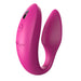The We-Vibe Sync Remote and App Controlled Wearable Couples Vibrator in Dusty Pink features a C-shaped design. One end has a ridged surface, while the other end is smooth, with a button and small logo on the smoother side. This couples' massager by We-Vibe is designed for intimate use.