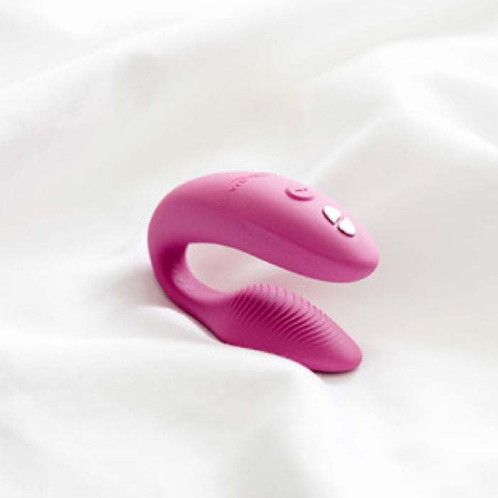 A Dusty Pink We-Vibe Sync Remote and App Controlled Wearable Couples Vibrator with both textured and smooth surfaces rests on a white fabric background. The top part of the device features visible buttons and controls, reflecting the innovative design characteristic of We-Vibe products.
