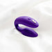 A purple, C-shaped silicone wearable couples' vibrator with dual ends and control buttons, resting on a white fabric surface. The We-Vibe Sync Remote and App Controlled Wearable Couples Vibrator - Purple by We-Vibe includes a wireless remote control for added convenience.