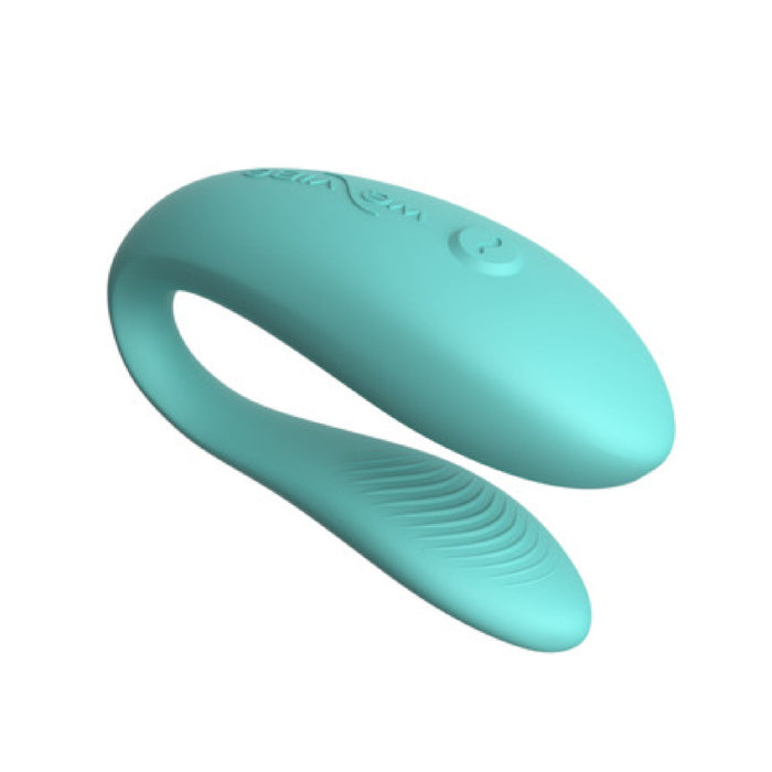The We-Vibe Sync Lite App Controlled Wearable Couples Vibrator in Aqua features a sleek, curved design with a single button on top. Its inner curve includes textured ridges for enhanced stimulation. This compact couples vibrator is ideal for solo play and offers the convenience of being controlled through the We-Vibe app.