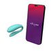 An aqua-colored, U-shaped We-Vibe Sync Lite App Controlled Wearable Couples Vibrator is positioned next to a smartphone with a screen displaying "We-Vibe" on a gradient red-to-purple background.