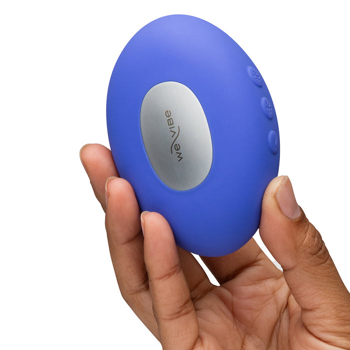 A hand holds the We-Vibe Temp Lay On Vibrator with Hot and Cold Functions, featuring a blue oval design, silver "We-Vibe" panel, and three side buttons, against a white background.