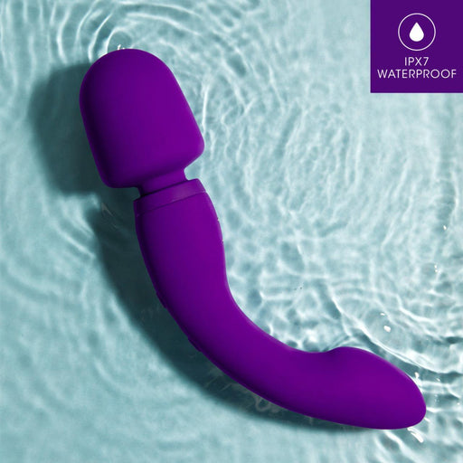 A purple Wellness Dual Sense Double Ended Ergonomic Waterproof Wand by Blush, designed for G-spot stimulation, rests on a light blue surface with rippling water. The top right corner of the image features a small label with an icon of a water drop and the text "IPX7 WATERPROOF" in white.