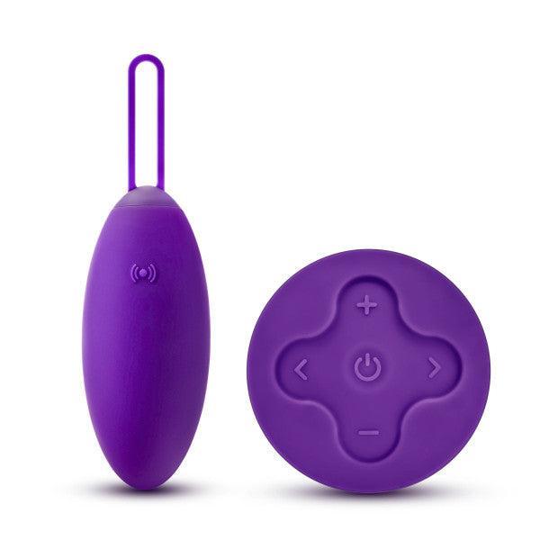 A purple Blush Wellness Imara Wearable Vibrating Egg with a matching wireless remote control. The remote, crafted in ultra silky silicone, boasts a rounded design and has four buttons featuring plus, power, minus, and wave symbols.