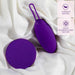 A purple Wellness Imara Wearable Vibrating Egg with Remote from Blush, featuring a loop handle, lies on a white fabric surface. Next to it is its matching round purple remote with control buttons. The image highlights the materials: Ultrasilk® smooth finish and PURIA® platinum-cured silicone, emphasizing its waterproof feature and wireless remote control functionality.