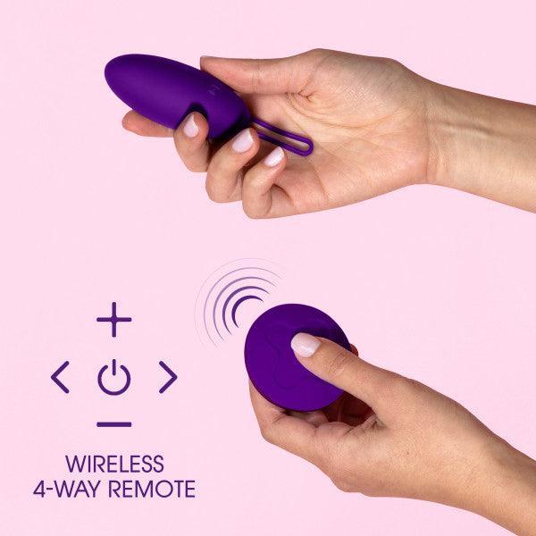 Two hands positioning the Blush Wellness Imara Wearable Vibrating Egg with Remote - Purple, showcasing its 10 vibration modes, while holding a circular remote control in the other hand. Text reads "Wireless 4-Way Remote" alongside directional arrows and remote symbols, all set against a light pink background.