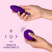 Two hands positioning the Blush Wellness Imara Wearable Vibrating Egg with Remote - Purple, showcasing its 10 vibration modes, while holding a circular remote control in the other hand. Text reads "Wireless 4-Way Remote" alongside directional arrows and remote symbols, all set against a light pink background.