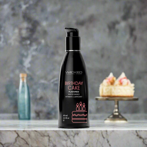 A black bottle of "Wicked Aqua Birthday Cake Flavored Water Based Lubricant" from Wicked Lubes, featuring a pump dispenser. The minimalist label showcases a birthday cake graphic and highlights that it is paraben-free, containing 60 ml (2.0 fl oz). Perfect for those who want to celebrate intimately with the delightful taste of Birthday Cake lube.