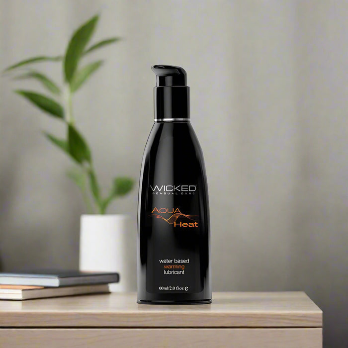 The Wicked Aqua Heat Water Based Warming Lubricant from Wicked Lubes comes in a sleek black 60ml (2 fl. oz) bottle featuring an orange design and text, along with a convenient pump dispenser on top. This water-based warming lubricant is sex toy friendly.