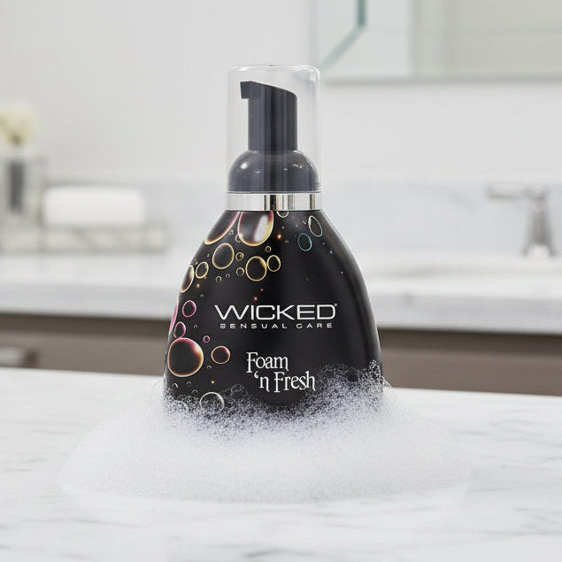 A bottle of Wicked Lubes' "Wicked Foam N Fresh Toy Cleaner 8oz." The dark container, decorated with vibrant bubbles, comes with a black pump dispenser. The label highlights its alcohol-free formula in white text and indicates a volume of 240ml/8 fl oz.