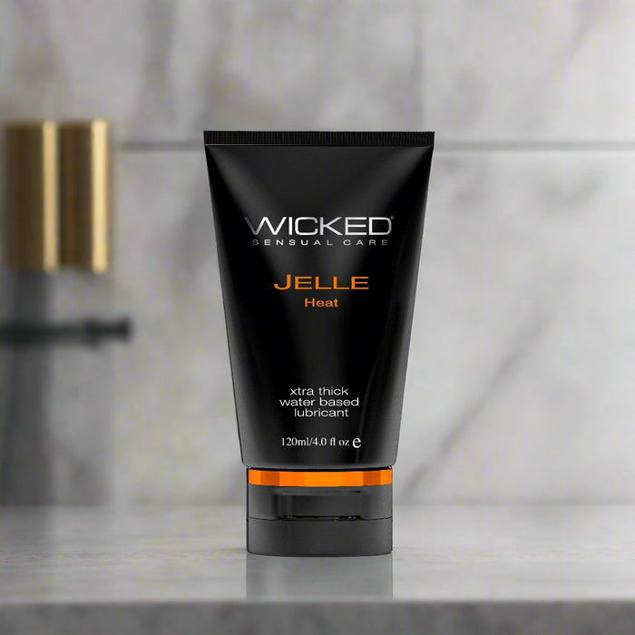 A tube of Wicked Jelle Heat Warming Anal Lubricant by Wicked Lubes is shown against a white background. The black tube has a flip-top cap and features orange and white text that reads "extra thick, extra long lasting water based lubricant," with the volume indicated as 120ml/4 oz.