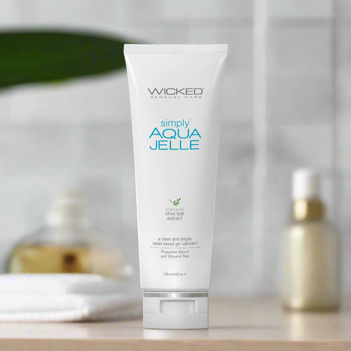 A white tube of "Wicked Simply Aqua Jelle Water Based Lubricant" by Wicked Lubes. The front label highlights the presence of olive leaf extract and specifies a content of 120 ml (4.0 fl oz). The tube stands upright against a plain white background.