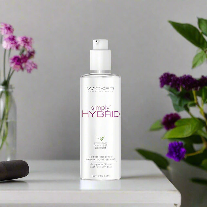 A bottle of Wicked Simply Hybrid Lubricant 4 oz by Wicked Lubes, with a white label and purple lettering. The bottle features a pump dispenser and contains 120 ml (4 fl. oz.) of product. Paraben-free and silicone-blended, it also boasts olive leaf extract and is described as creamy and hybrid.