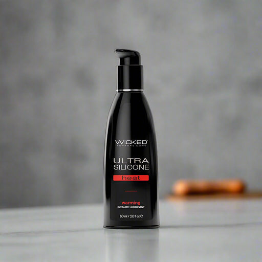 A black bottle of Wicked Ultra Heat Warming Silicone Lubricant 2 oz by Wicked Lubes with a pump dispenser. The label reads "Wicked Ultra Silicone Heat Warming Intimate Lubricant 60 ml / 2 fl oz" in white and orange text. This sleek, modern bottle delivers the ultimate experience in vegan sex products.