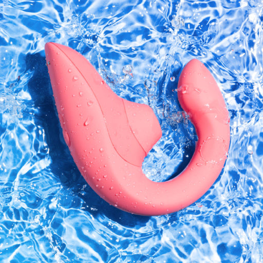 The Womanizer Blend Pleasure Air Clitoral & G-Spot Rabbit - Rose, a waterproof and curved silicone vibrator from Womanizer, floats in clear blue water. The ripples surrounding the toy accentuate its sleek design and smooth texture, ideal for dual stimulation.