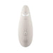 The Womanizer Premium 2 Pleasure Air Clitoral Stimulator in Warm Gray by Womanizer is a sleek, modern handheld device with an elliptical shape that features multiple buttons on its front surface. These include a power button, a wave symbol button for adjusting the Pleasure Air settings, and plus and minus buttons for fine-tuning.