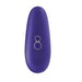 The Womanizer Starlet 3 Pleasure Air Clitoral Stimulator - Indigo by Womanizer is a sleek, oval-shaped, purple handheld electronic device. It features two small circular buttons labeled with plus and minus symbols, and utilizes Pleasure Air Technology for clitoral stimulation. The device is USB rechargeable and has a small emblem at the bottom with two tiny holes at the top.