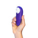 A hand holding the Womanizer Starlet 3 Pleasure Air Clitoral Stimulator in Indigo, a small purple handheld device by Womanizer with a white circular attachment at one end, against a plain white background.