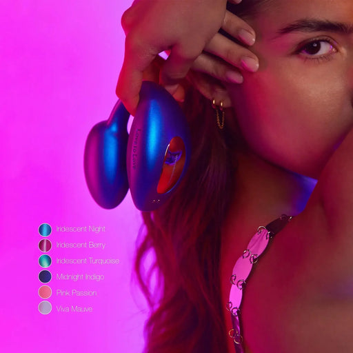 A person holds a deep blue, pear-shaped wearable remote control vibrator from Lovely Planet's Wonderlover collection near their head against a vibrant pink-purple background. At the left, six color options are listed: Iridescent Night, Iridescent Berry, Iridescent Turquoise, Midnight Indigo, Pink Passion, Viva Mauve.