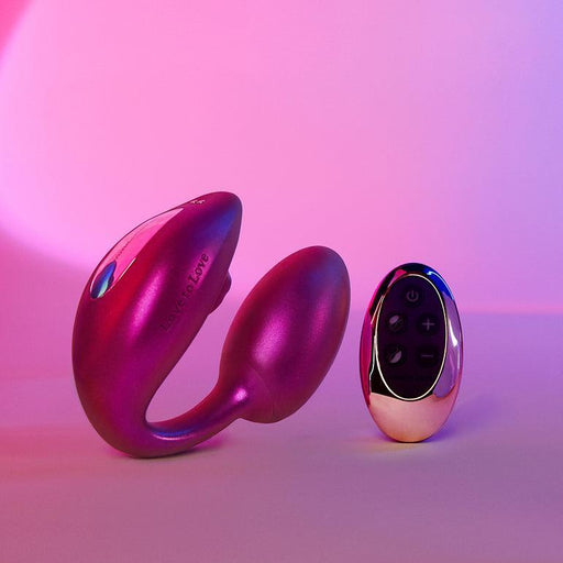 The Wonderlover Hands Free Clitoral and G-Spot Vibrator with Remote by Lovely Planet, a pink wearable vibrating sex toy designed for G-spot stimulation, and its matching remote control are displayed on a surface with a pink and purple gradient background. The toy features two ergonomic parts for intimate use, while the remote offers multiple buttons to explore various settings.