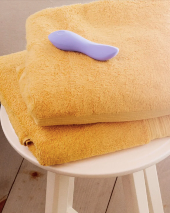 Dame Dip Beginner's  Internal & External Silicone Vibrator - Periwinkle sitting on a yellow towel placed on a wood stool