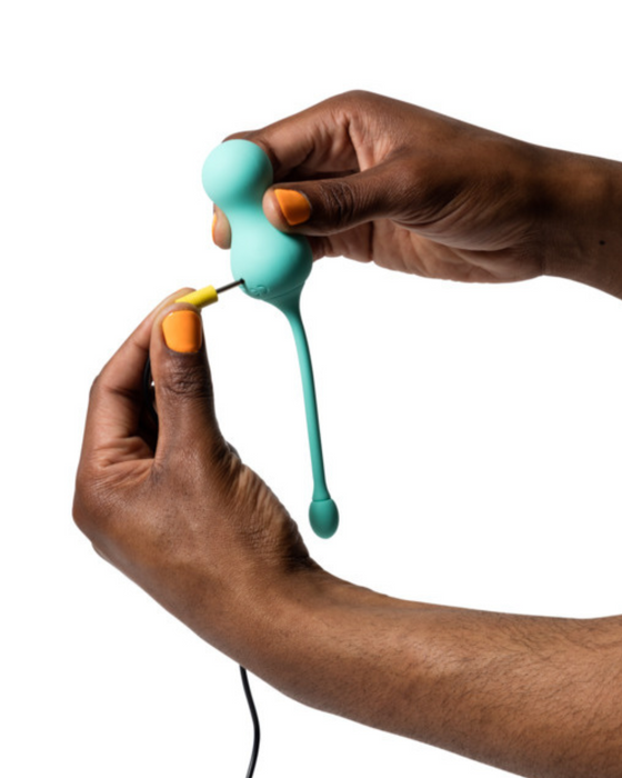Romp Cello Remote Control G-spot Vibrating Egg being held by a hand and the other showing where the charging cord  plugs in. On a white background