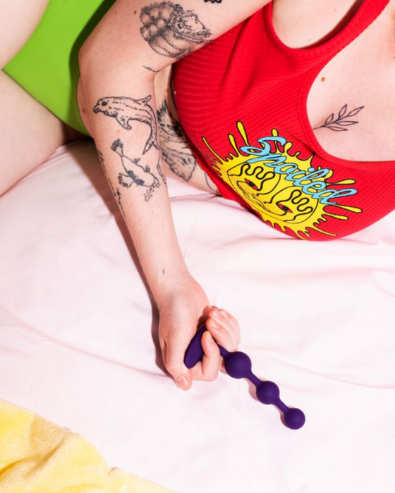 Romp Amp Flexible Anal Beads being held by a tattooed model on a bed
