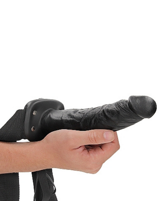Black Realrock 8 Inch Hollow Dildo & Strap-on Harness being held by a hand on a white background