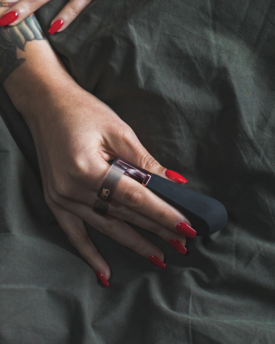 Hot Octopuss Digit Silicone Rechargeable Finger Vibrator held by a woman  with long nails on a black silk sheet