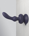 An ergonomic, dark-colored silicone Pipedream Products Wall Banger Vibrating Rechargeable Prostate & Anal Plug with Suction Cup door stopper attached to a light-colored tiled wall, providing a cushion to prevent doorknob impact.