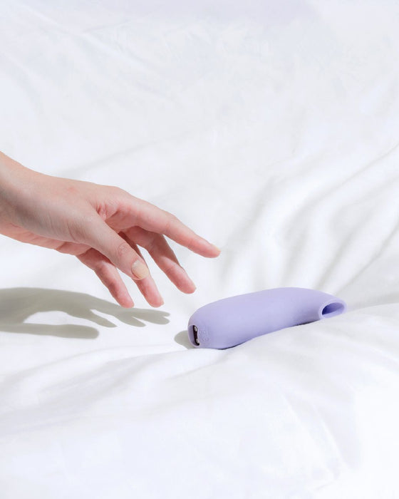 Aer Clitoral Suction Toy Vibrator by Dame Products  hand reaching for product on bed 