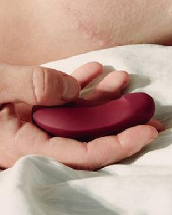 Dame Pom Hand Held Flexible Vibrator - Plum held in a person's palm against a white sheet