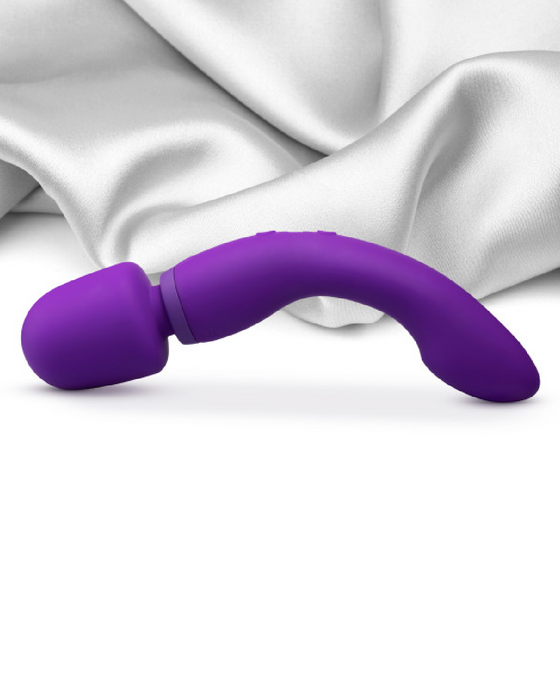 A purple curved Blush Wellness Dual Sense Double Ended Ergonomic Wand placed on a silky white fabric surface.