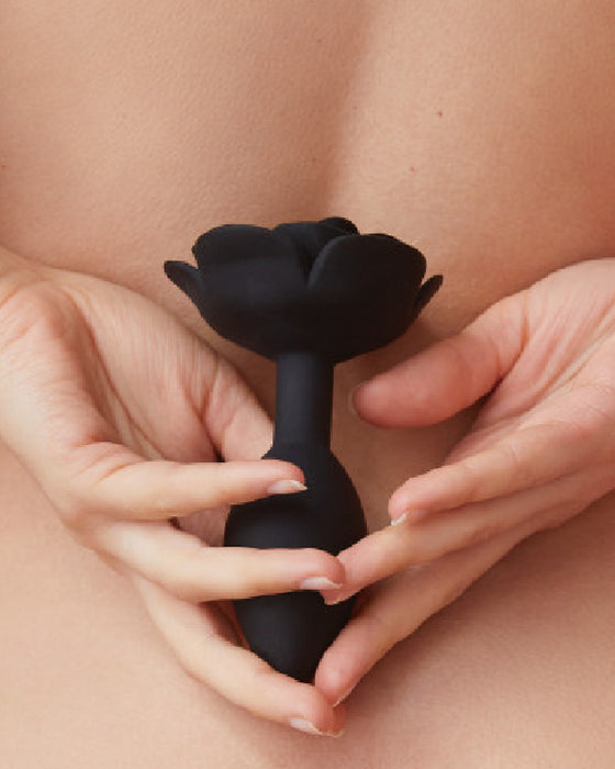 Open Roses Large Silicone Anal Plug - Black held in a woman's hand behind her back