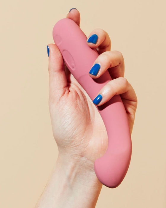 Dame Arc Silicone Waterproof G-Spot Vibrator held in a hand with blue nail polish, tip facing downwards