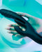 A hand in a black glove holding an Evolved Novelties Rapid Rabbit Thrusting Vibrator with Flapping Shaft against a contemporary cyan backdrop.