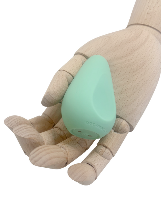 A wooden mannequin hand gently cradling a mint green, triangular-shaped Ritual Chi Palm Sized Ergonomic Soft Silicone Bullet Vibrator by Doc Johnson.